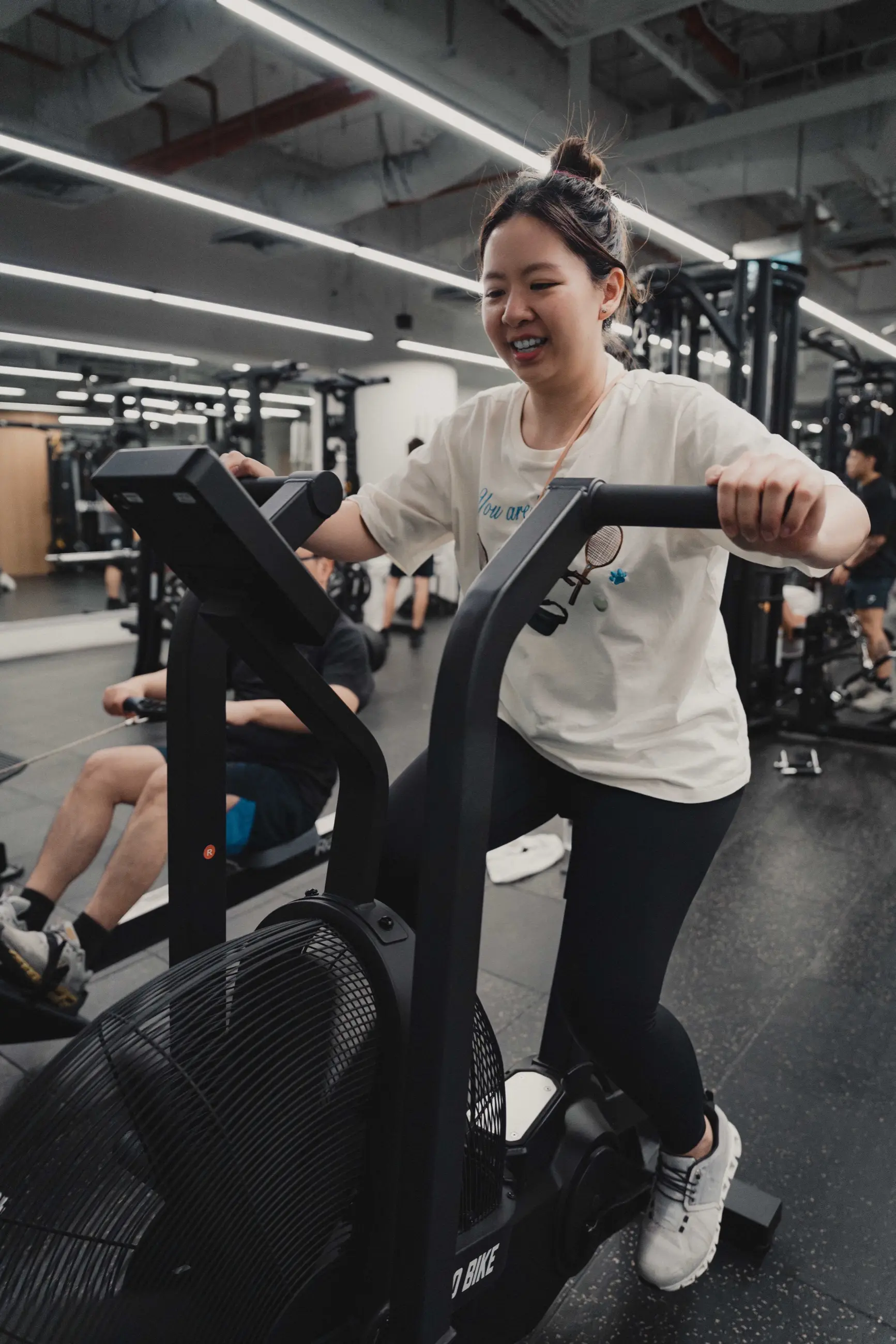 A client smiling through a hard effort on the air bike during a coached session on the Forge & Flow training floor