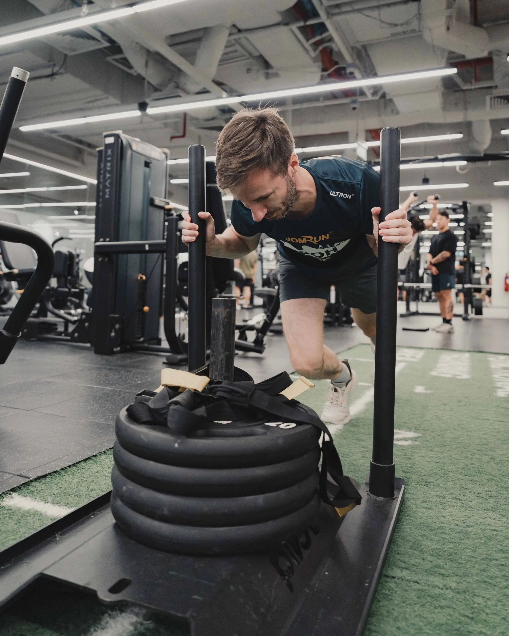 A participant drives a weighted sled along the turf during a coached session
