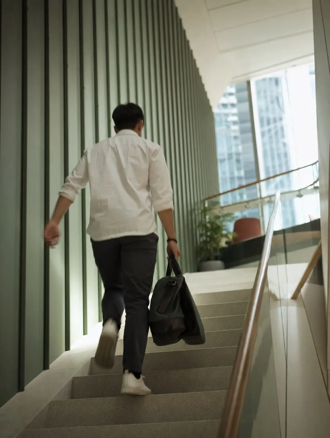 A person climbing an office stairwell carrying a holdall